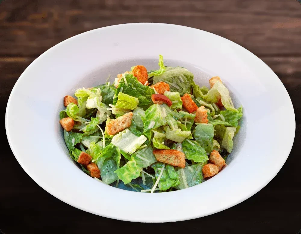 Top-down Caesar salad in white bowl with croutons and dressing.