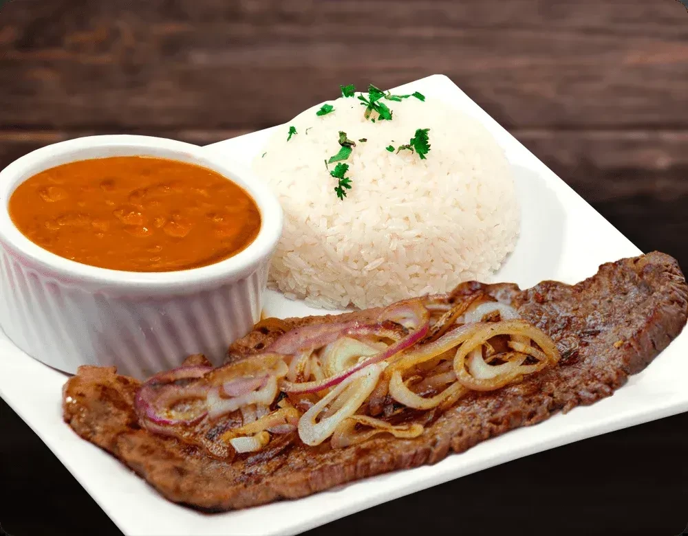 Steak with sautéed onions, white rice, and beans on a white plate.