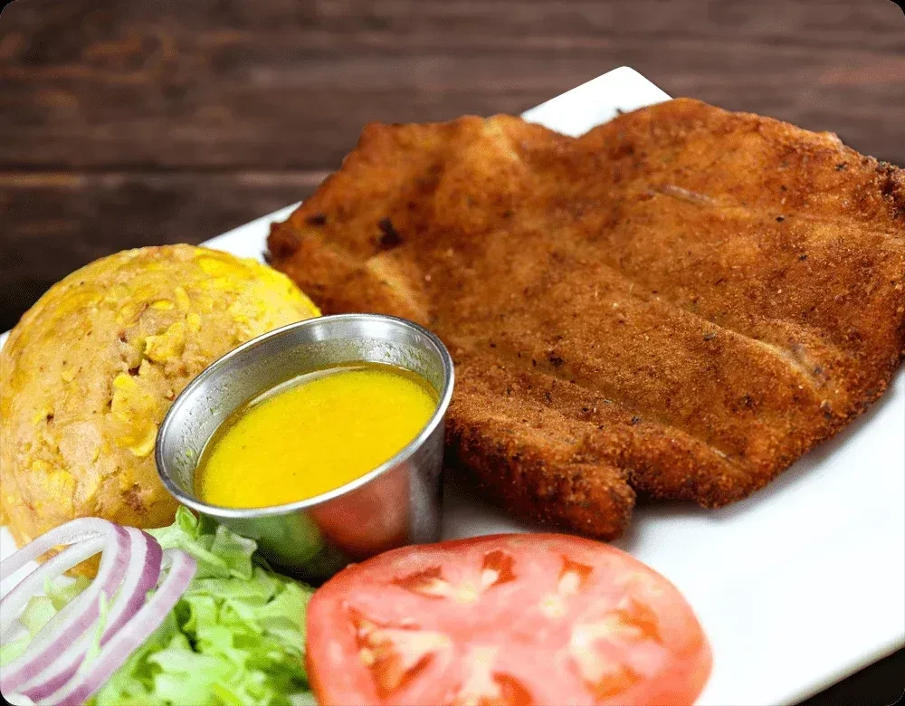Meal with golden fried cutlet, mashed plantain, sauce, and salad.