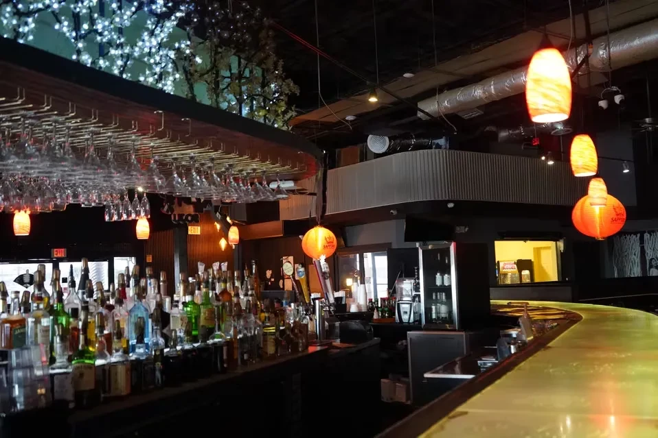 Dimly lit modern bar with stocked shelves, hanging glasses, and decorative lanterns.