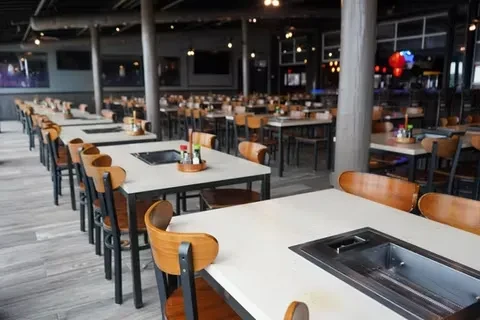 Empty modern-industrial Korean BBQ restaurant with tables and grills.