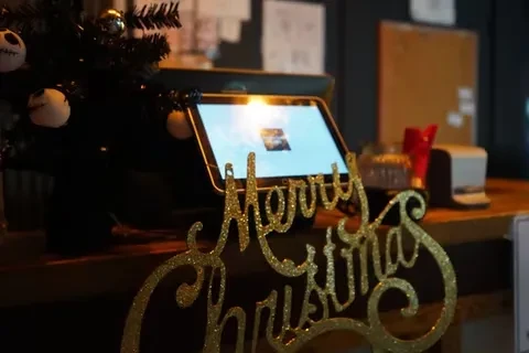 Golden 'Merry Christmas' sign, Jack Skellington tree, and tablet on bar counter.