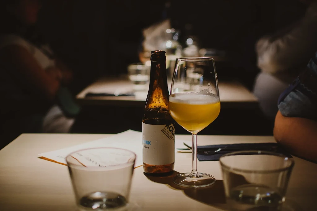 Condensing amber beer bottle and glass on a dimly lit restaurant table.