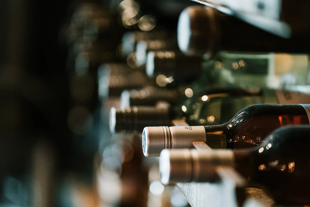 Close-up of horizontal wine bottles on a dim rack, focused on caps.