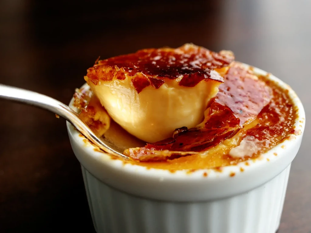 Crème brûlée in white ramekin with spoon breaking caramelized sugar crust.