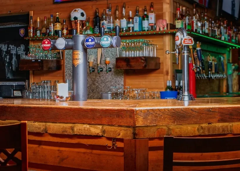 Rustic wooden bar counter with beer taps and liquor bottles.