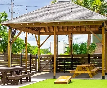 Outdoor wooden gazebo with picnic tables and cornhole game.