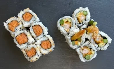 Spicy tuna maki and tempura shrimp sushi rolls on a dark surface.