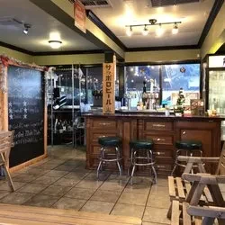 Empty casual bar interior with wooden counter, stools, and Sapporo sign.