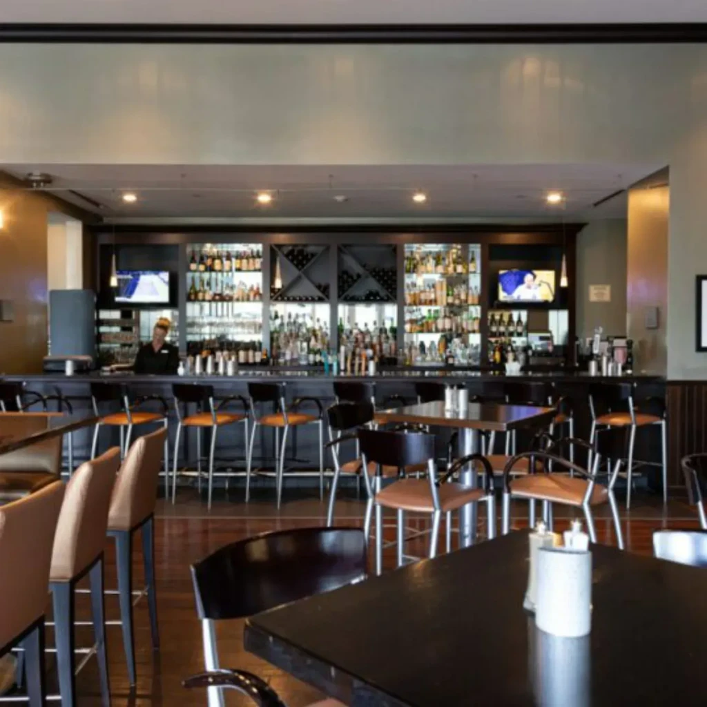 Well-stocked contemporary bar interior with dining tables and a bartender.
