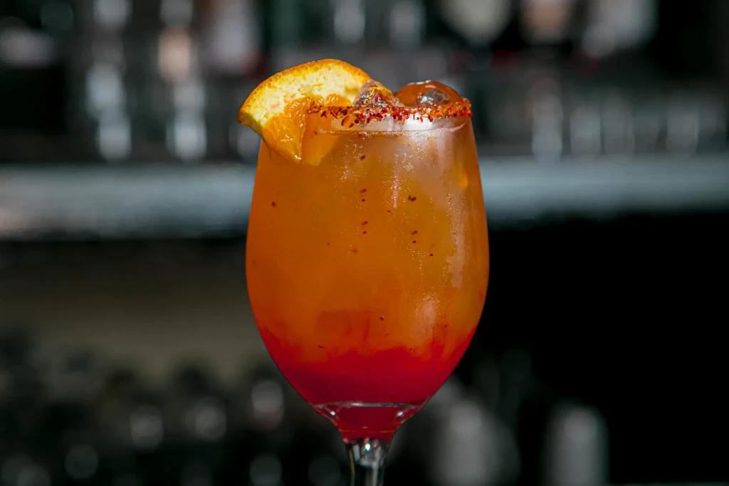 Colorful gradient cocktail in wine glass with chili-lime rim and orange slice.