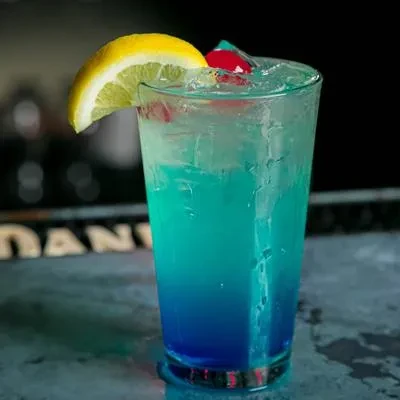 Blue and teal layered cocktail with ice, lemon, and cherry.