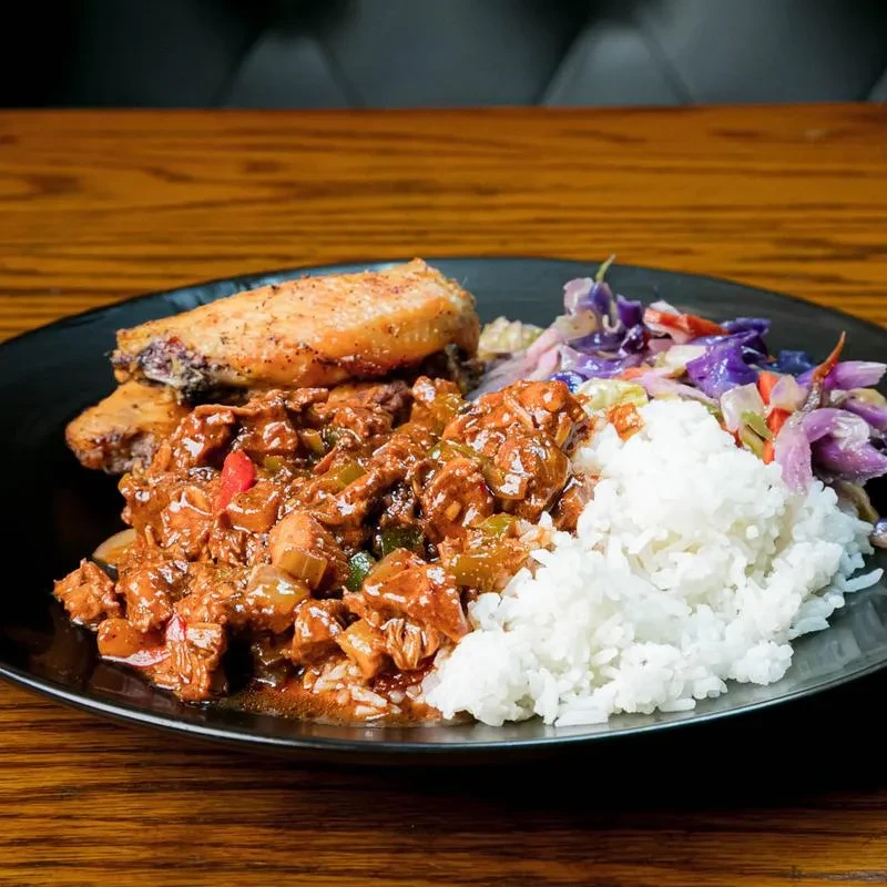 Plate of rice, meaty stew, coleslaw, and two pieces of fried chicken.