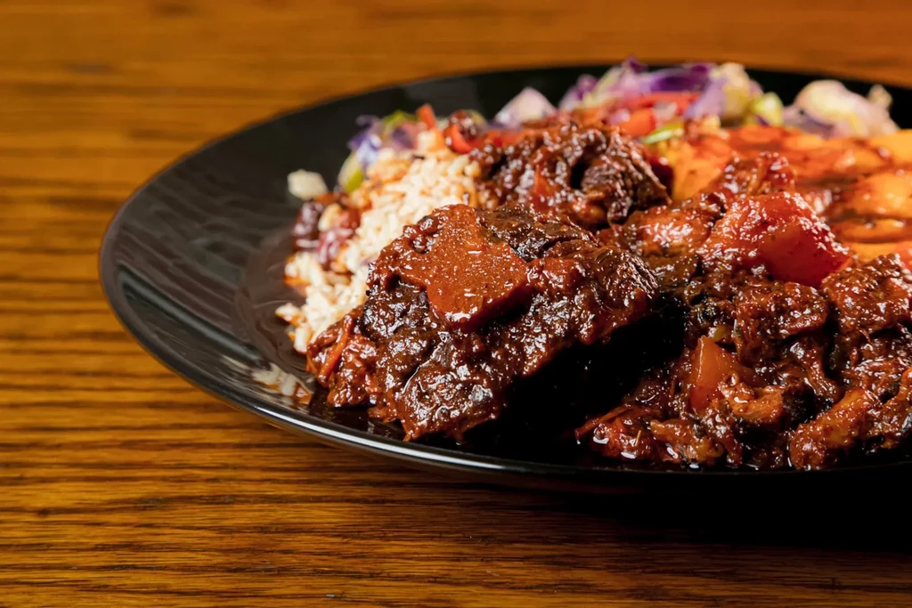 Hearty stew, rice, and colorful salad on black plate, wood table.