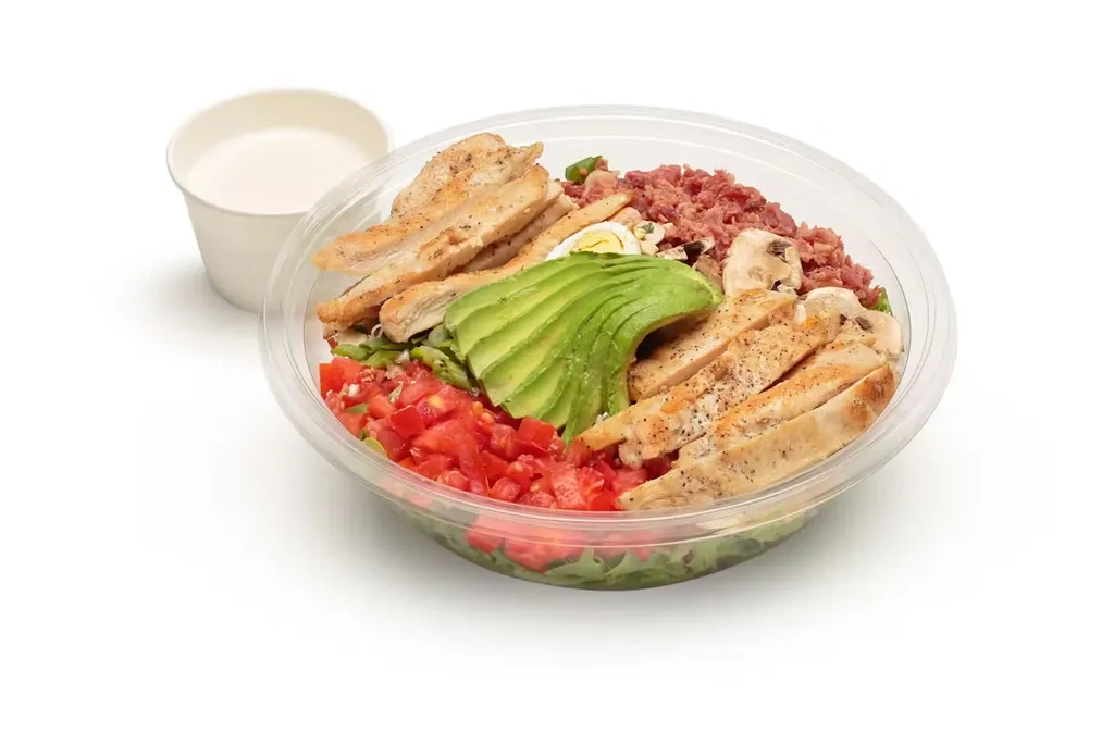 Grilled chicken salad with avocado, bacon, tomatoes, mushrooms, egg, and dressing.