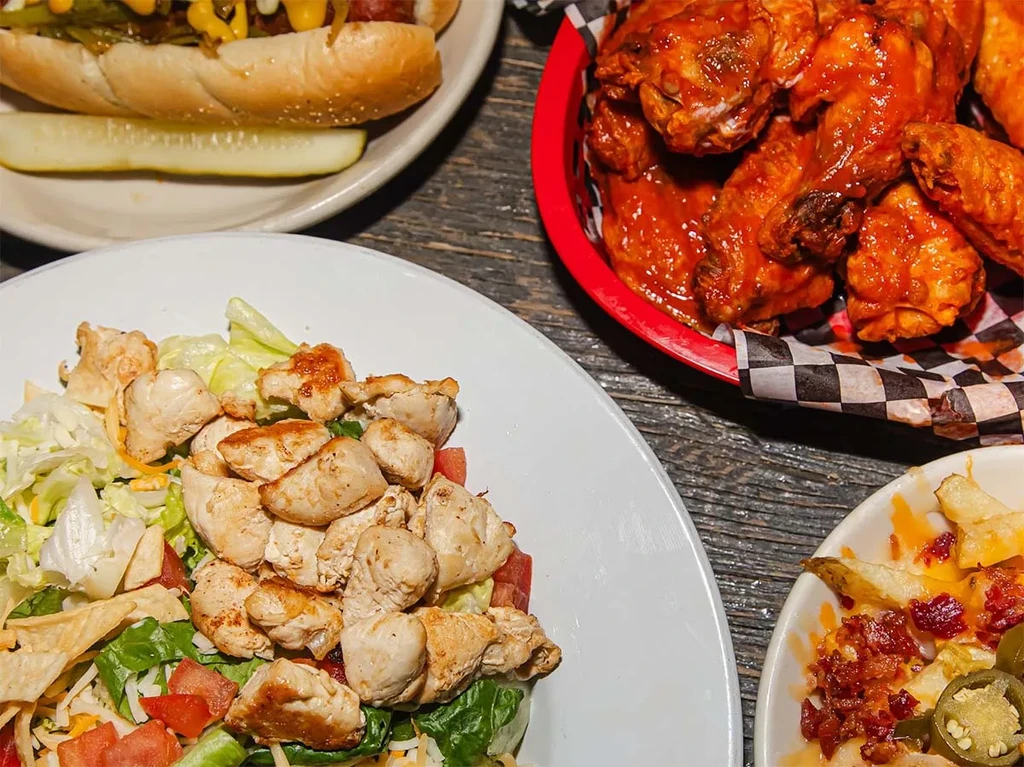 Overhead shot of chicken salad, hot dog, wings, loaded fries.