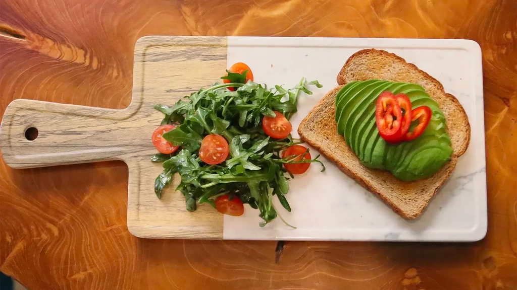 Avocado toast with chili and arugula salad on a serving board.