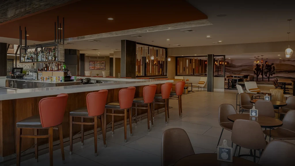 Empty modern restaurant bar with orange stools, lounge seating, and desert mural.