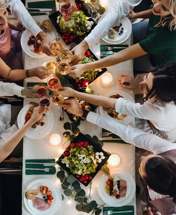 Overhead, a group toasts wine glasses at a warm, candlelit table.