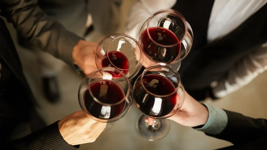 Overhead shot of four hands clinking red wine glasses.