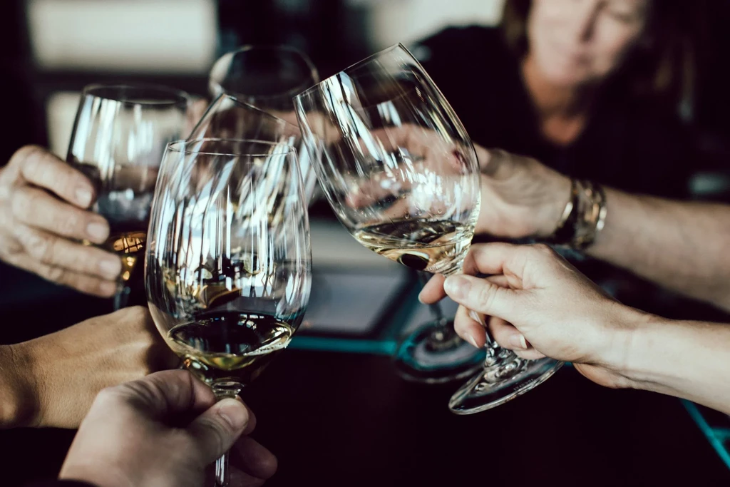 Four hands clinking wine glasses with white wine.