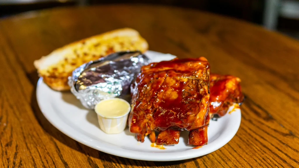 Plate of saucy barbecue ribs, baked potato, and garlic bread.