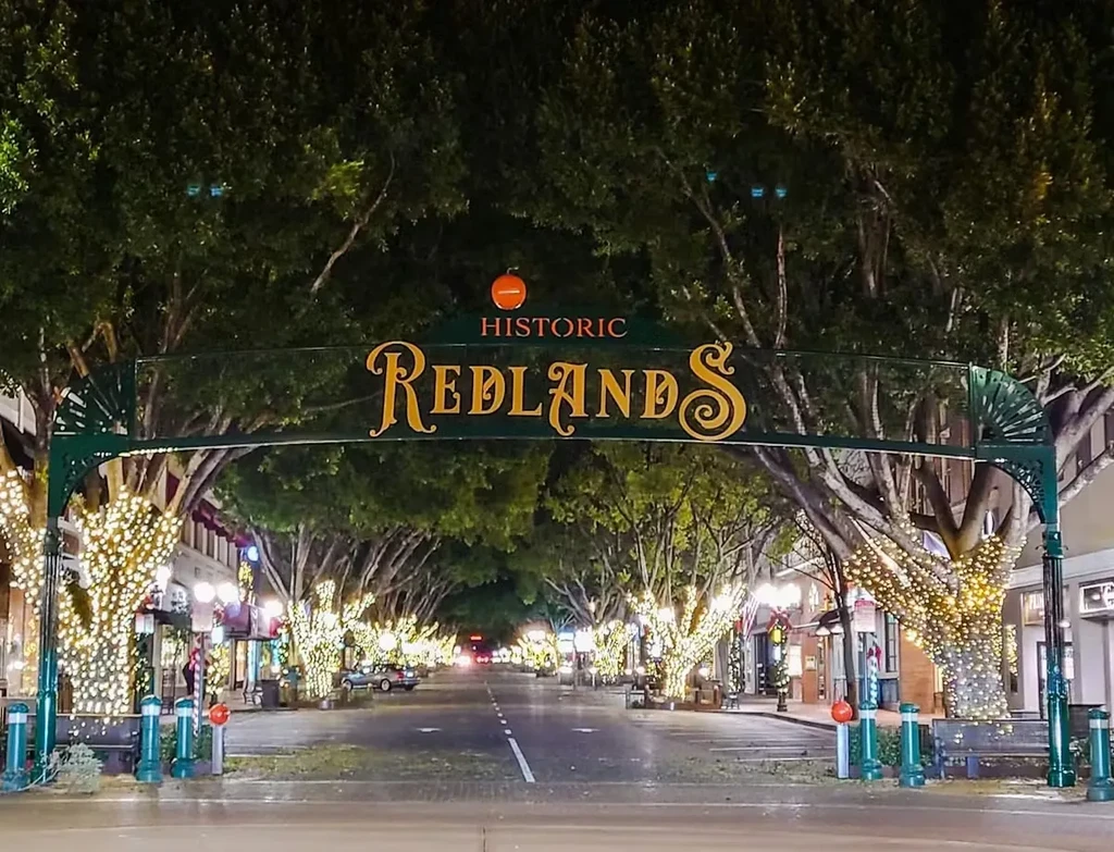 Historic Redlands archway spans a downtown street with string-lit trees at night.