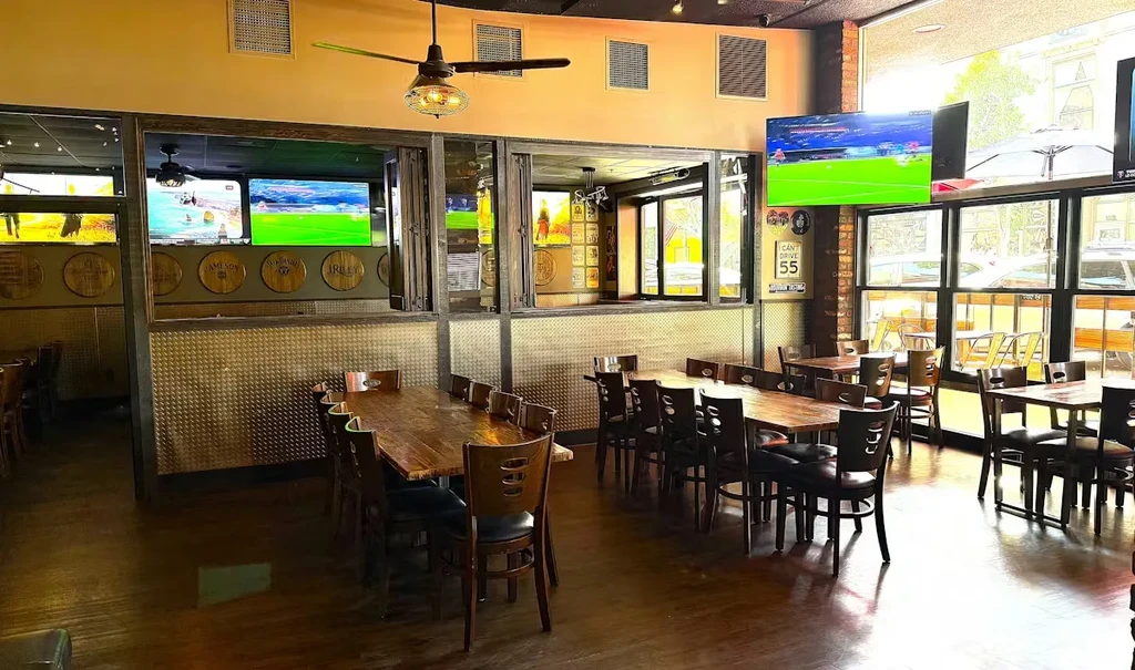 Empty casual restaurant interior with wooden tables and TVs showing sports.