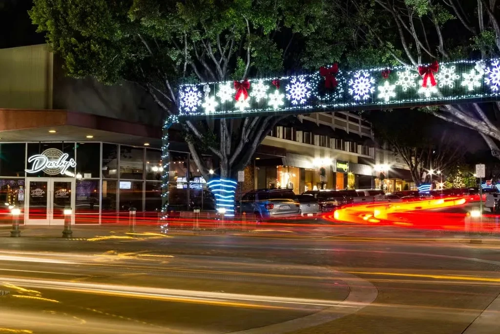 Holiday-decorated night street with Darby's restaurant and long exposure light trails.