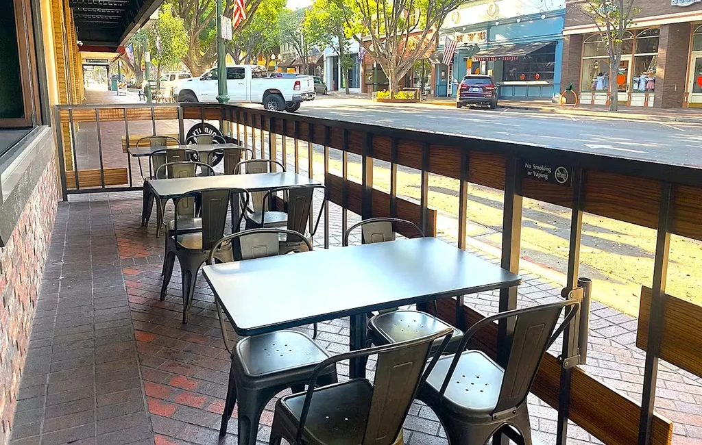 Empty outdoor restaurant patio with tables, chairs, and "No Smoking" sign.