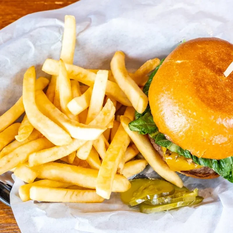 Hamburger with cheese, lettuce, and golden french fries in a basket.