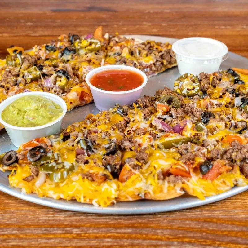 Loaded taco pizza with meat, cheese, vegetables, and sauces on a pan.