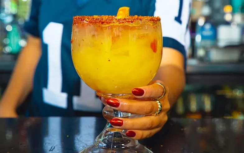 Yellow-orange drink in stemmed glass, spiced rim, citrus wedge.