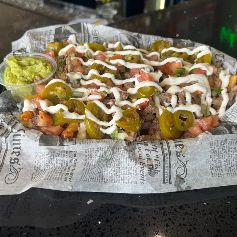 Loaded fries with meat, tomatoes, jalapeños, white sauce, and guacamole.