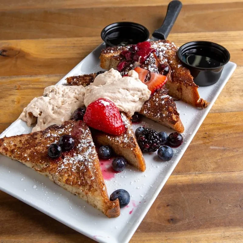 French toast with berries, whipped cream, and syrup on a rustic table.