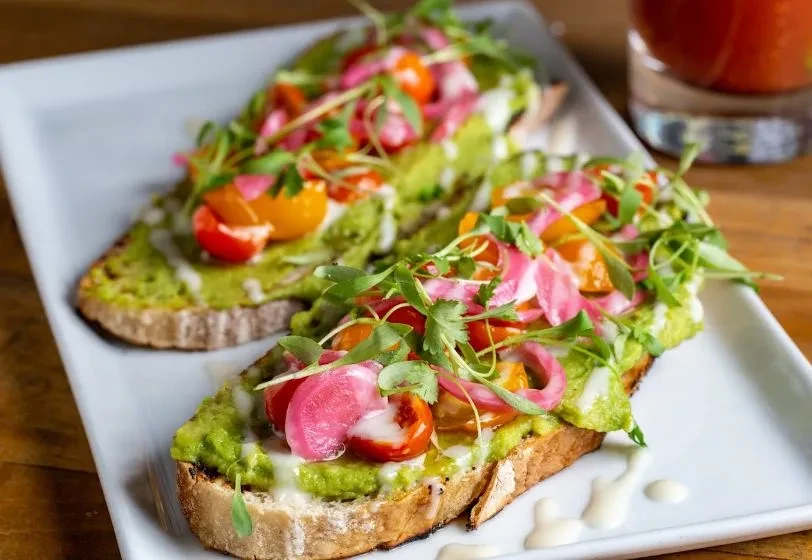 Two slices of avocado toast with tomatoes, pickled onions, microgreens.