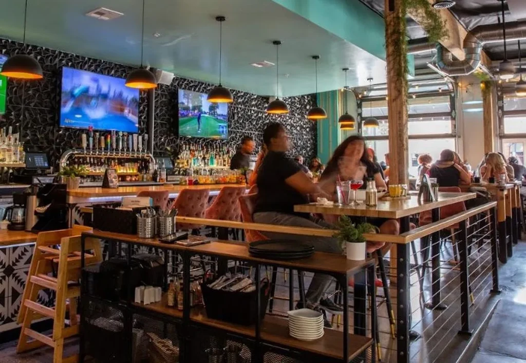 Lively restaurant bar interior with patrons, drinks, and sports.