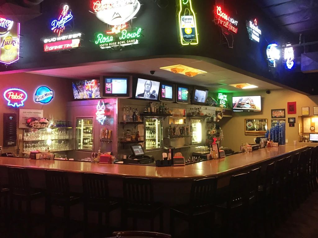 Well-equipped sports bar with L-shaped bar, neon signs, and TVs.