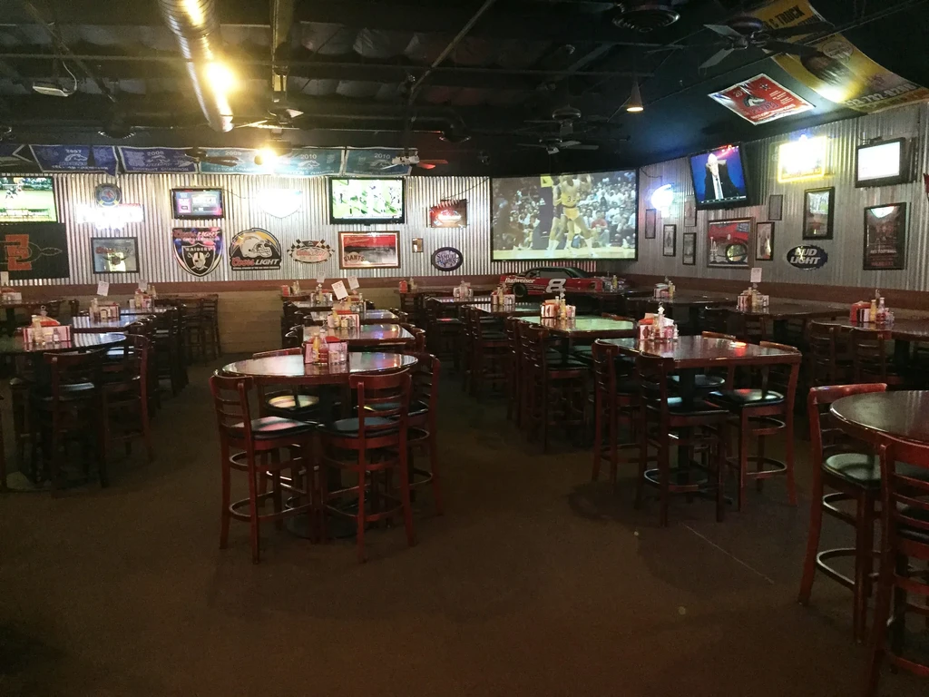 Empty sports bar interior with dark wood, TVs, and sports memorabilia.