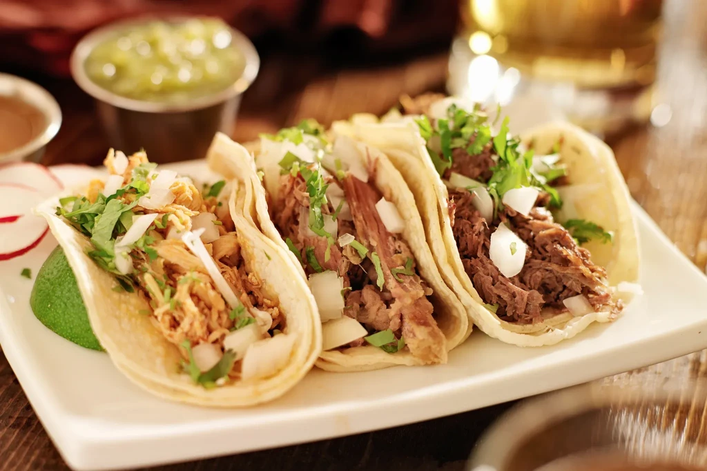 Three soft-shell tacos, shredded meat, onions, cilantro, lime, and radish.