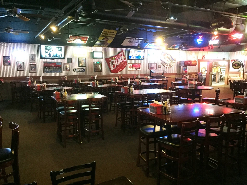 Interior of a dimly lit sports bar with high-top tables and TVs.