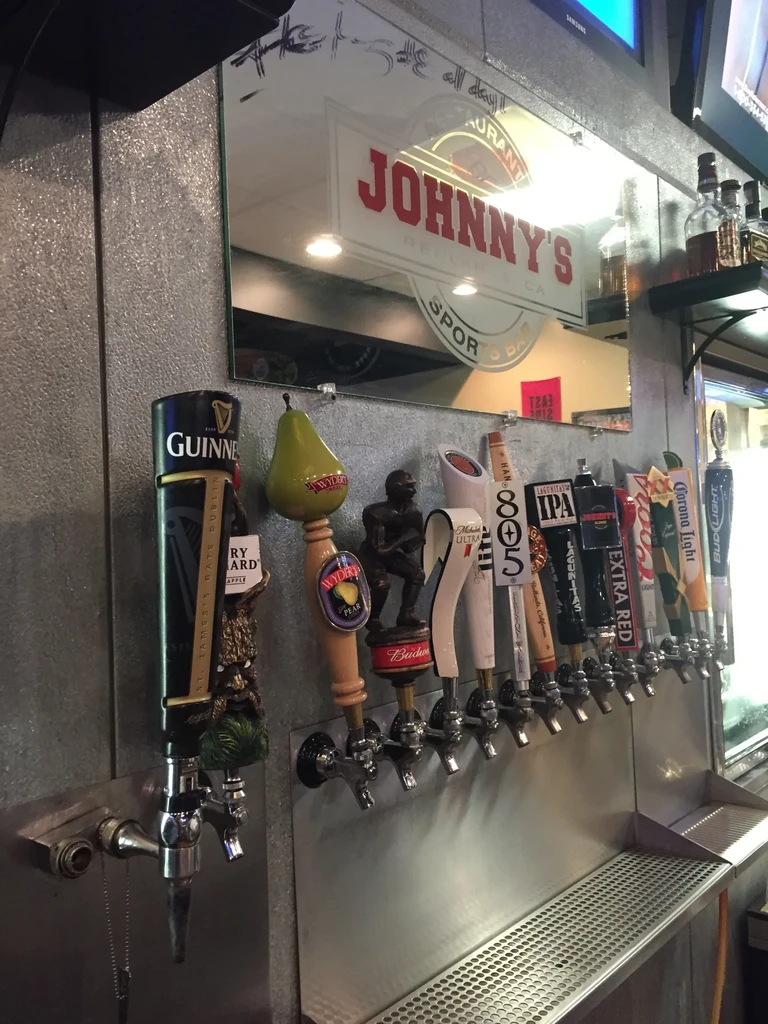 Row of beer taps reflecting "Johnny's Restaurant Sports Bar" sign.