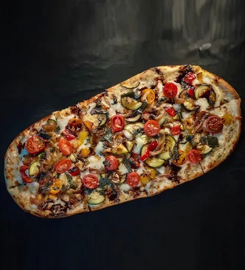 Gourmet flatbread pizza with zucchini, colorful tomatoes, basil, balsamic drizzle.