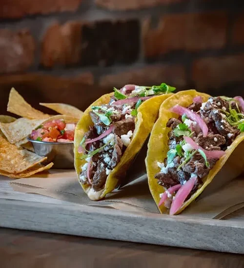 Two beef tacos, salsa, and tortilla chips on a wooden board.
