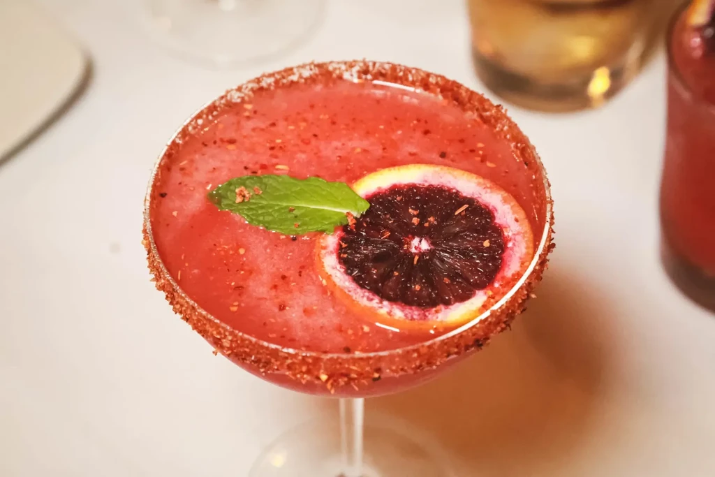 Red slushy cocktail with spiced rim, mint, and blood orange garnish.