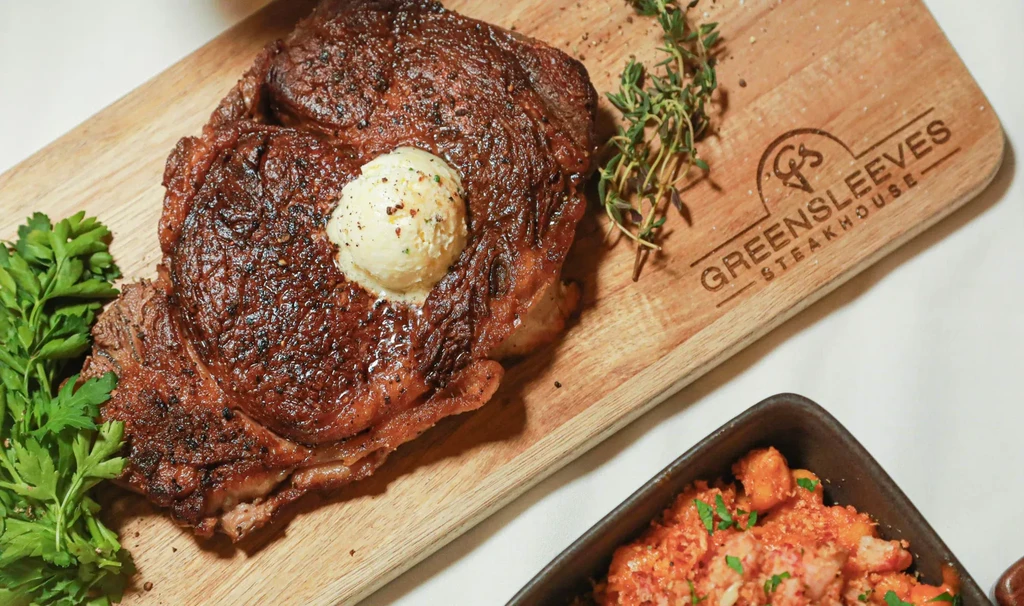 Glistening steak with melting butter, herbs, on a wooden board.