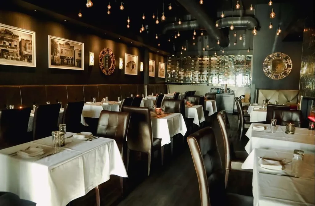 Empty upscale dining room with white tables, leather seats, and Edison bulbs.