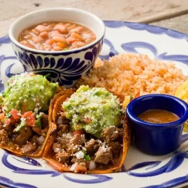 Colorful plate of two Mexican tacos, rice, pinto beans, and salsa.