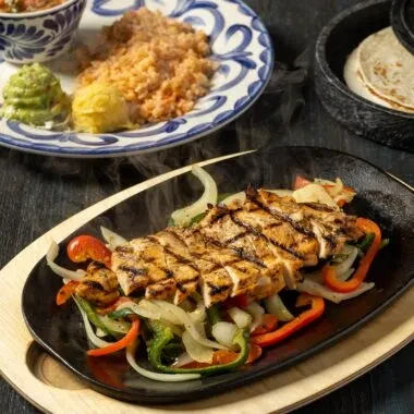 Sizzling grilled chicken fajitas with peppers, onions, rice, and tortillas.