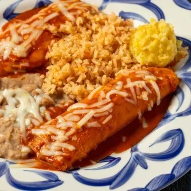 Two cheesy enchiladas, Spanish rice, and refried beans on a plate.